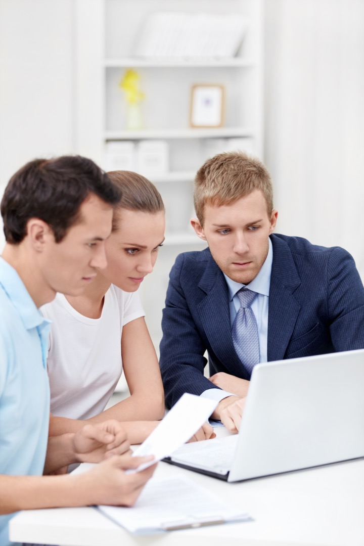 Un consultant et ses clients regardant un rapport d'assurance sur un laptop.